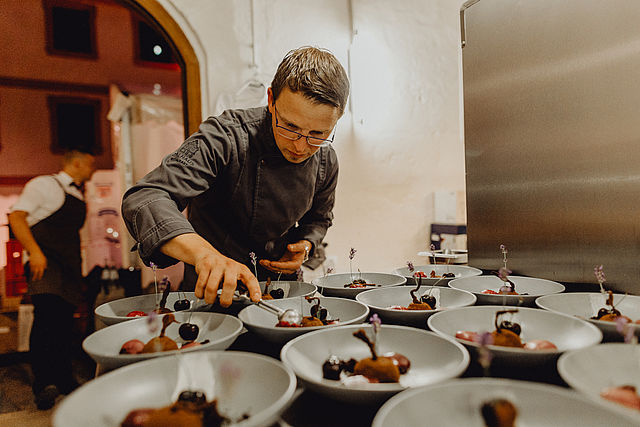 Ein Koch richtet auf weißen Tellern ein Dessert an.