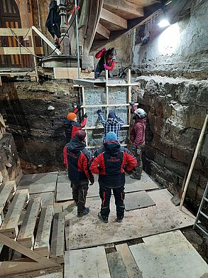 Das fertige Sedimentstransferpräparat wird von mehreren Arbeitern und der Künstlerin vorsichtig von den Gesteinsschichten gelöst.