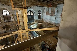 Innenansicht einer riesigen Halle mit Großbaustelle. In der Mitte wurde eine deckenhohe Stützen mit Holzpfählen abgestützt.