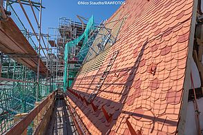 Ein Dach wird mit rot-orangenen Dachziegeln neu eingedeckt.