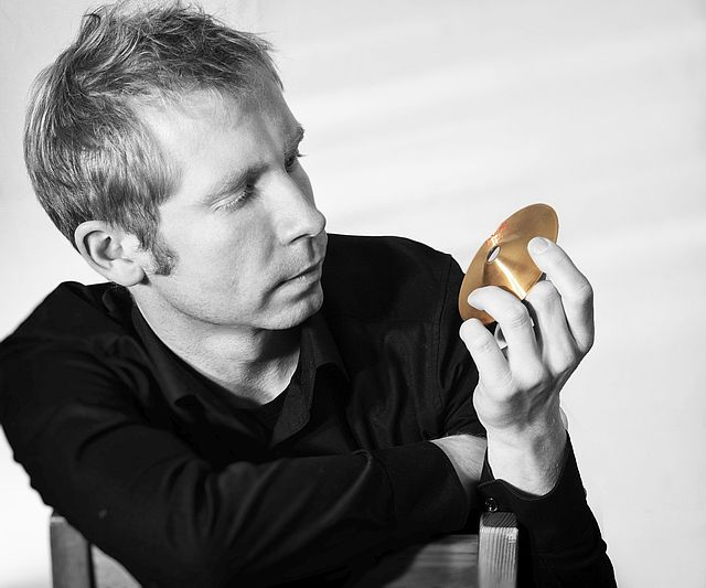 Hochschulprofessor Radoslaw Szarek hält ein goldenes Musikinstrument in seiner Hand fest und schaut es an 
