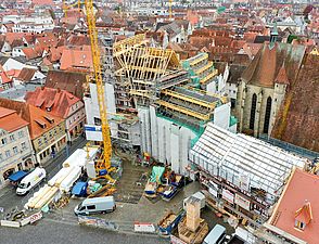 Eine Luftbildaufnahme zeigt ein historisches großes Gebäude in einer Stadt. Das Gebäude ist mit einem Gerüst und großen Planen umgeben.