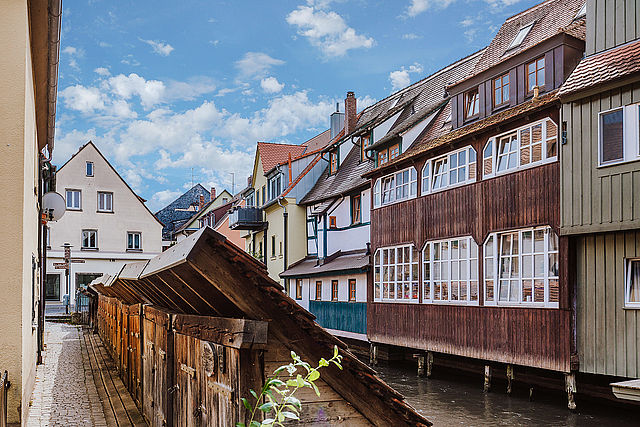 Stadtansicht bei sonnigem Wetter mit Blick auf die Wiesent, den angrenzenden Fischkästen aus dunklem Holz und der historischen Häuserfassaden am Fluss.