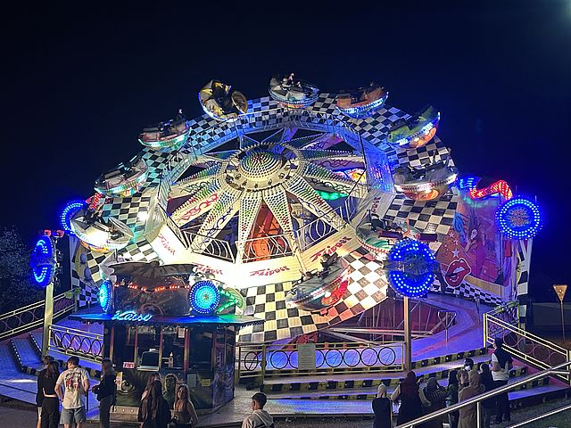 Ein beleuchtetes Fahrgeschäft mit sich drehenden Gondeln in der Nacht.