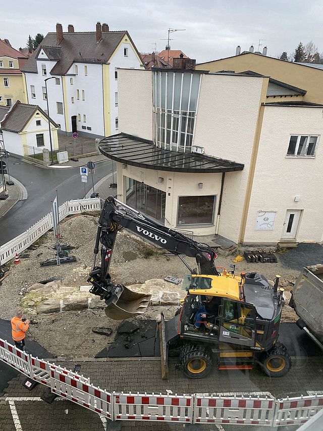Aus der Vogelperspektive ist die Baustelle in der Wallstraße zu sehen. Ein Bagger entfernt die obere Straßendecke. Das Areal ist mit rot-weißen Bauzäunen abgesperrt.