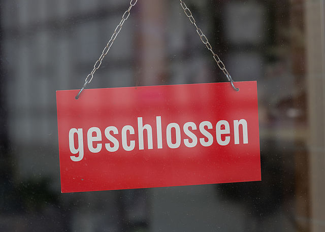 Ein rotes Schild mit dem Wortlaut geschlossen hängt an einer Glasscheiben, an der sich schemenhaft Fachwerkgebäude spiegeln.