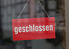 Ein rotes Schild mit dem Wortlaut geschlossen hängt an einer Glasscheiben, an der sich schemenhaft Fachwerkgebäude spiegeln.