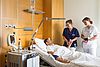 Kranker im Pflegebett mit zwei Krankenpflegepersonen