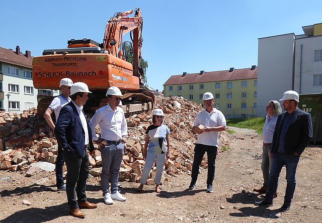 Die Baustelle in der Paul-Keller-Straße mit Bagger und 7 Personen im Vordergrund.