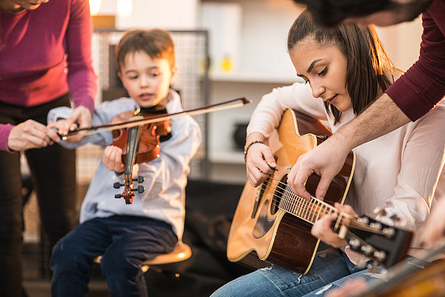 Kinder spielen Instrumente, ein Junge Geige und ein Mädchen Gitarre.