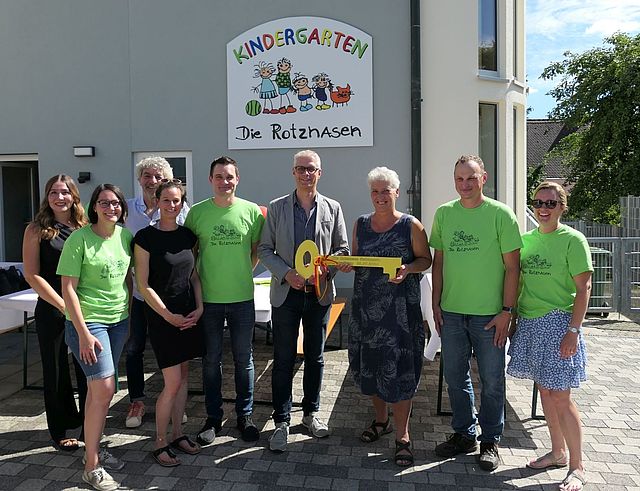 Eine Gruppe von Personen steht mit einem symbolischen Schlüssel vor einem Gebäude.