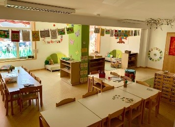 Ein bunt möblierter Spielraum mit Tischen in Gruppen, Spieleregalen und Girlanden mit selbstgemalten Bildern.